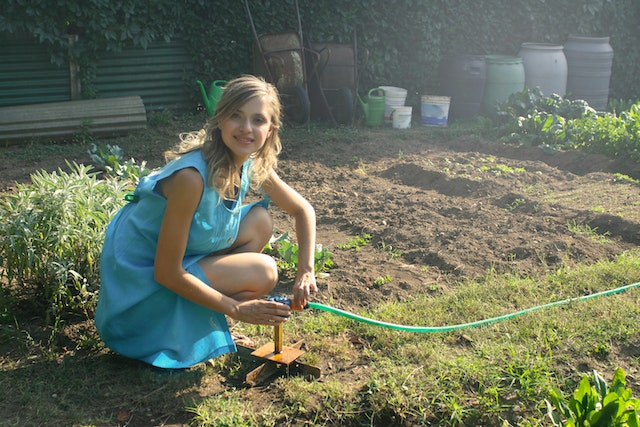 A young woman crouched in her garden as she sets up a sprinkler system.