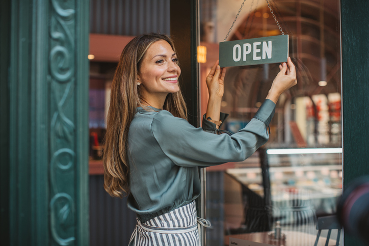 Female business owner flips a sign to "Open" on the door to her shop.