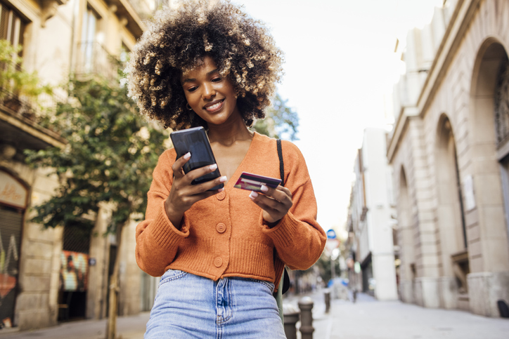 Young woman smiles while typing her credit card number into her phone.