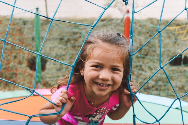 Little girl with brown hair smiles for the camera as she plays on a playground.