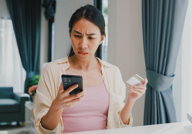 Woman looks at her phone with a concerned face while she holds a credit card.