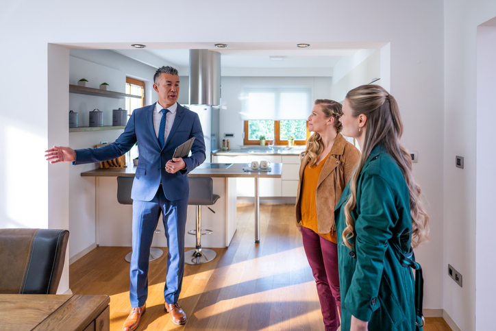 Two females stand opposite a male real estate agent wearing a suit as they view a home for sale.
