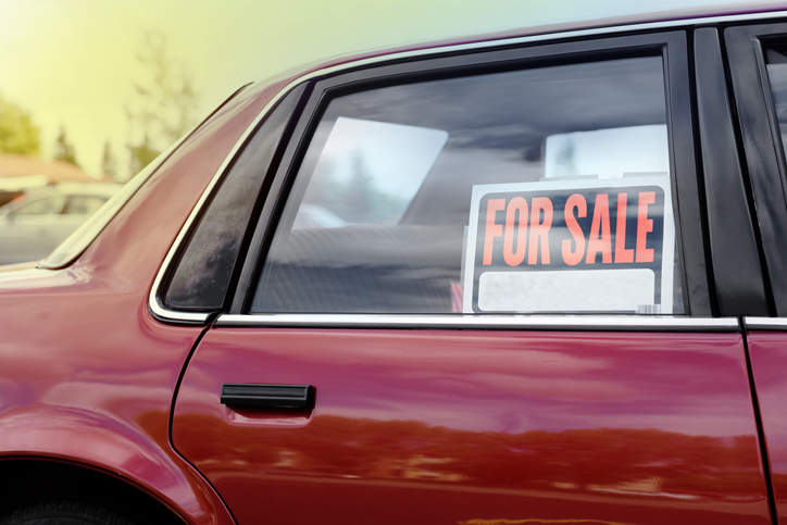 An older-model, red four-door car with a "For Sale" sign in the window.
