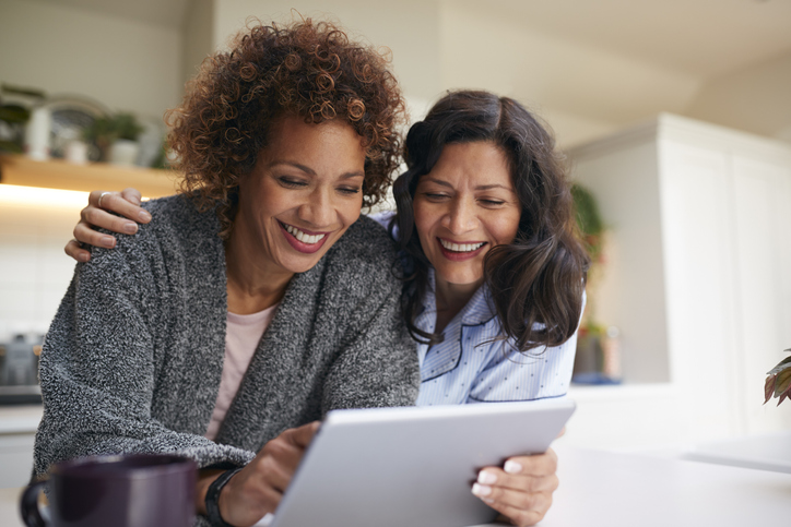 Two women smiling while looking at a tablet.