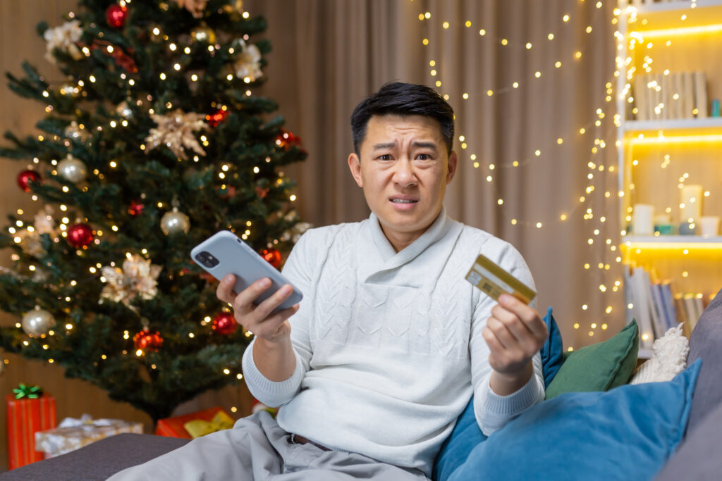 Man sitting in front of a Christmas tree with a flustered expression on his face.