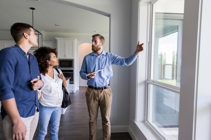 Real estate agent gesturing out a window while talking to a man and woman.