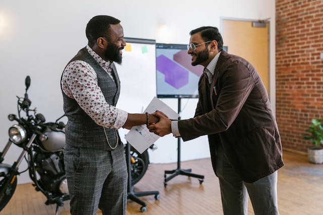 Two men in suits smiling while shaking hands.
