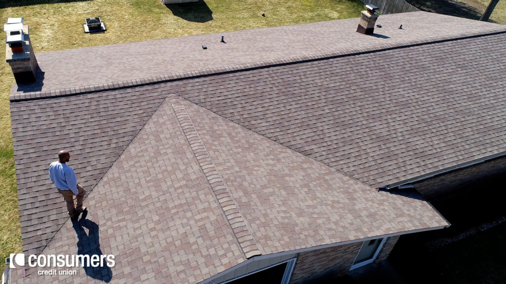 An aerial view of a man on a house roof inspecting the shingles.