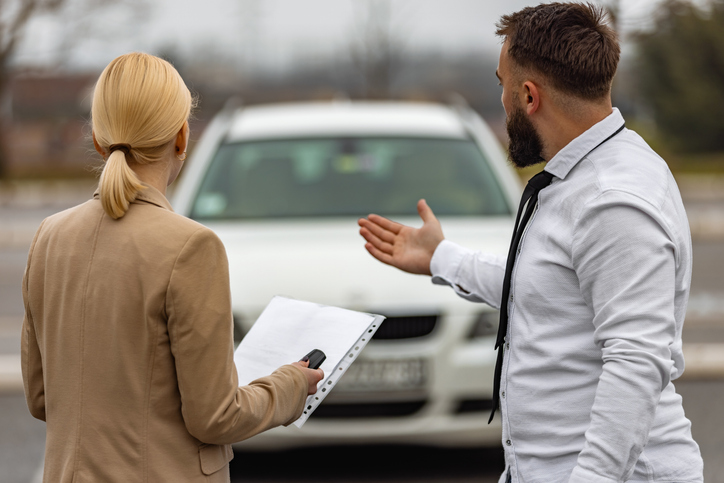 Man and woman facing away from the camera and looking at a car with a document and the keys in hand.
