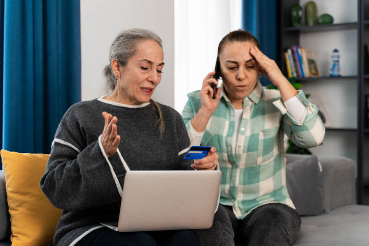 Senior woman and another woman stressed while talking on the phone and on a laptop.