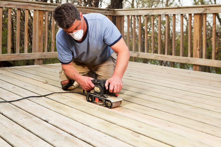 Man sanding down planks on his deck.