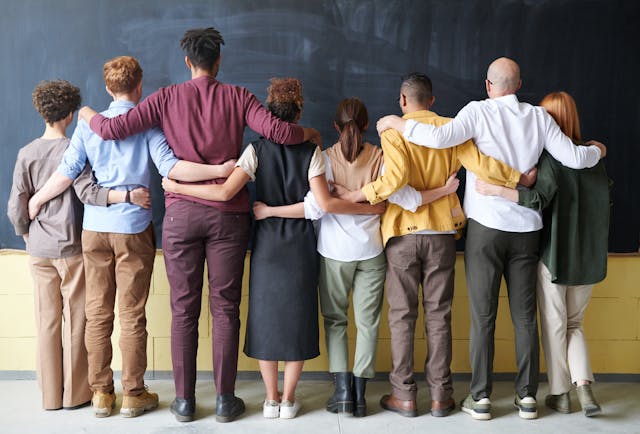 Coworkers of various age and race standing together with their arms around each.