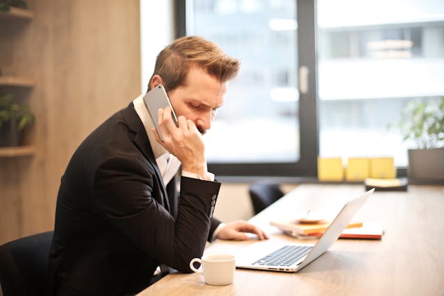 Man looking frustrated while on the phone and sitting in front of a laptop.
