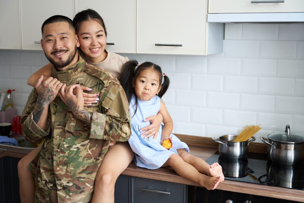 Military family hugging each other and smiling in a kitchen.