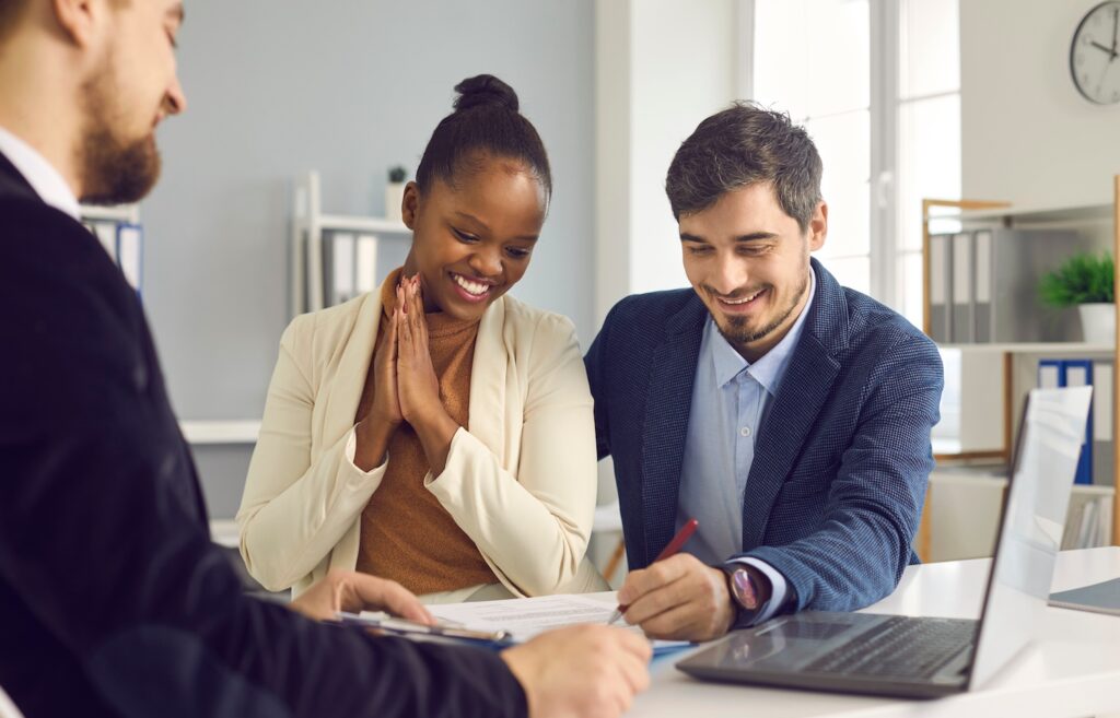 Man and woman sitting together and smiling while going over paperwork with a financial professional.