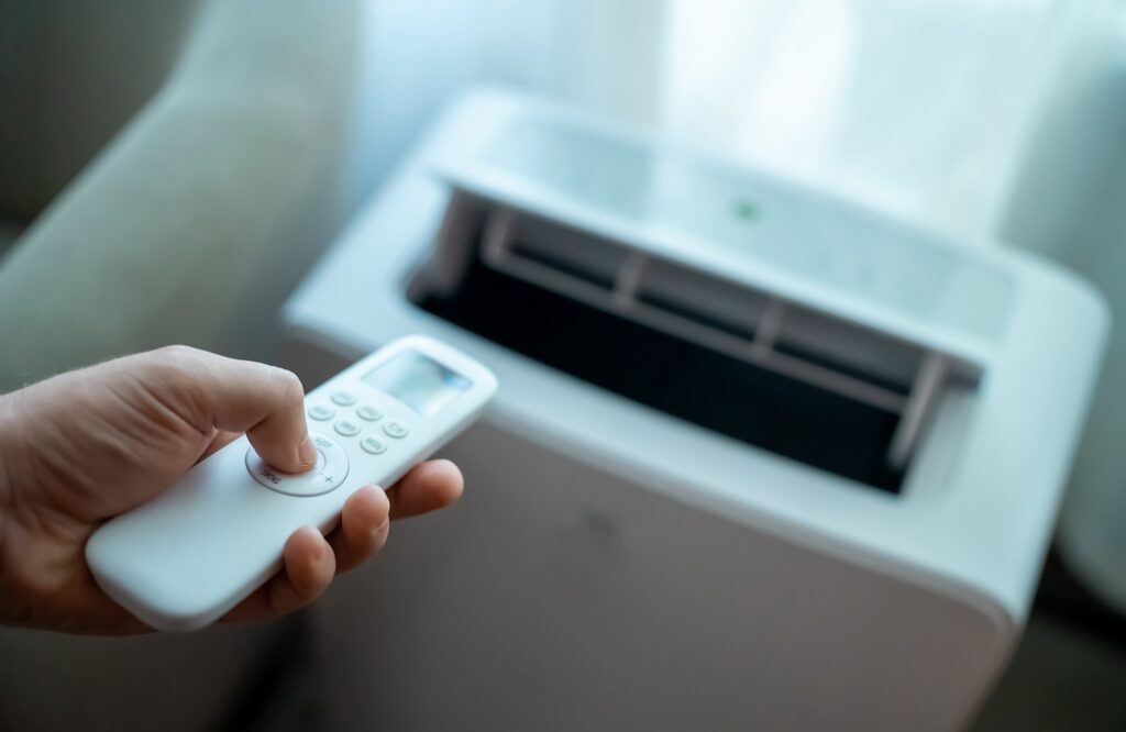 Hand holding a remote controller pointed at a portable air conditioner.