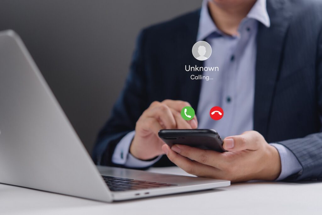 Man sitting in front of his laptop getting a phone call from an unknown caller on his cell phone.