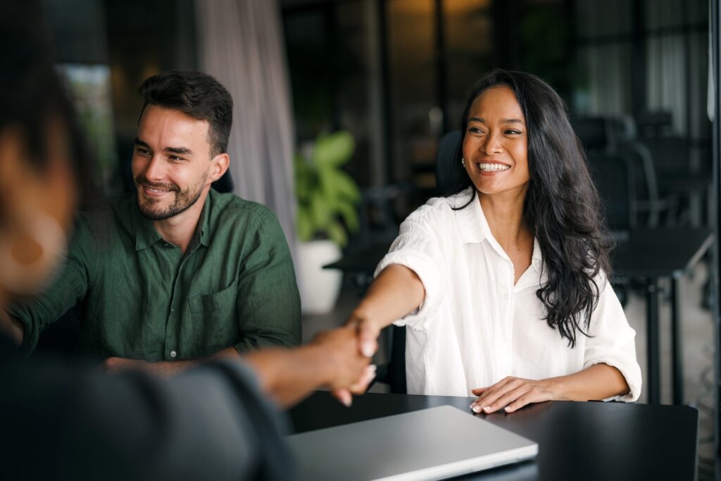 Man and woman smiling while shaking hands with another person.