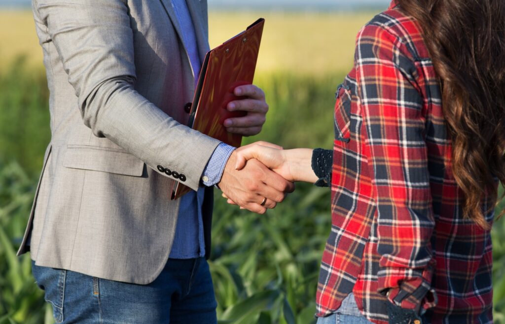 Farmer and businessman shaking hands in front of a field.