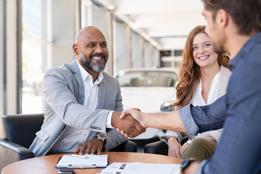 Couple shaking hands with a salesman at a car dealership.