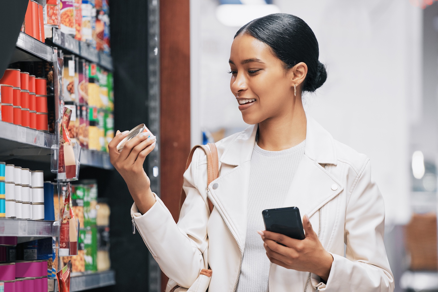 Young woman smiling while shopping in a supermarket and holding her phone.
