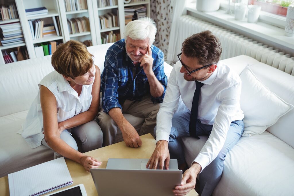 Mature couple sitting with a financial advisor and looking at a laptop.
