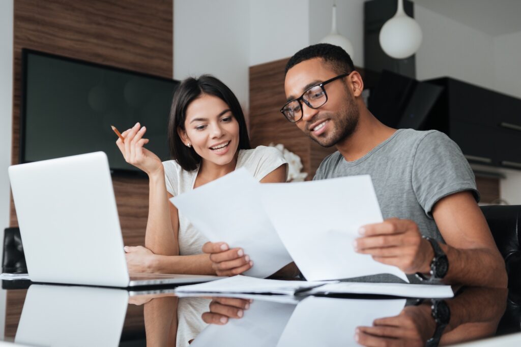Man and woman smiling while looking over paperwork in front of a laptop.