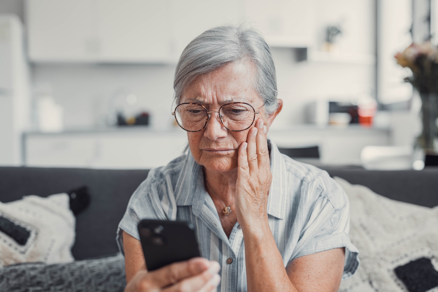 Mature woman sitting on the couch looking confused at her phone.
