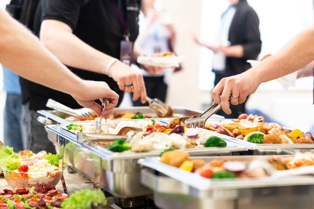 Hands picking up food from a catered buffet.