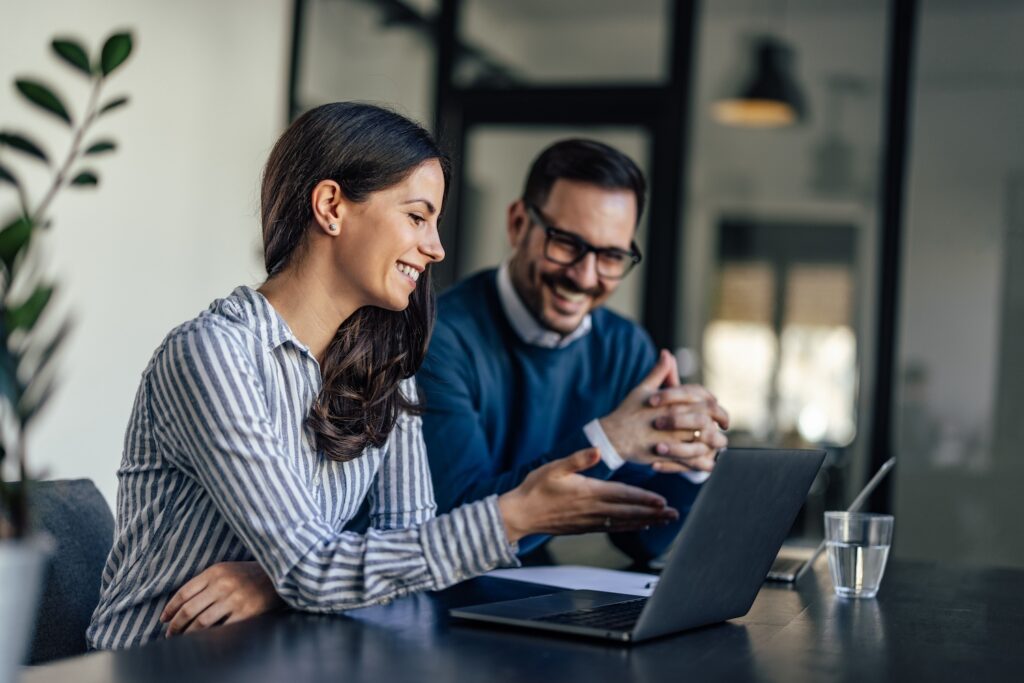 Two people sitting together and looking at a laptop while smiling.