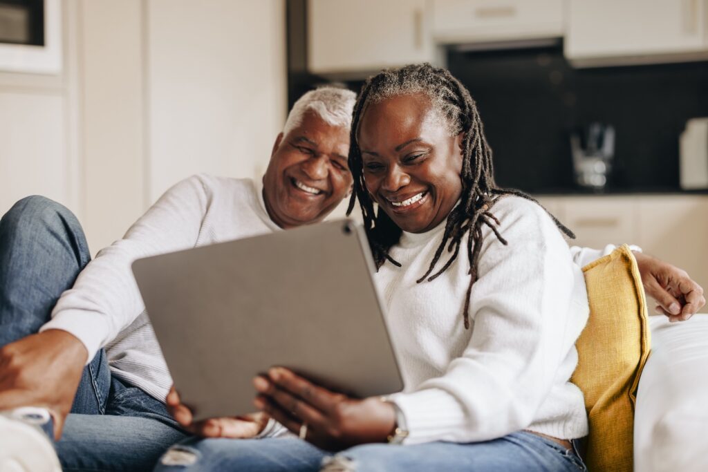 Mature couple smiling while looking at a tablet.