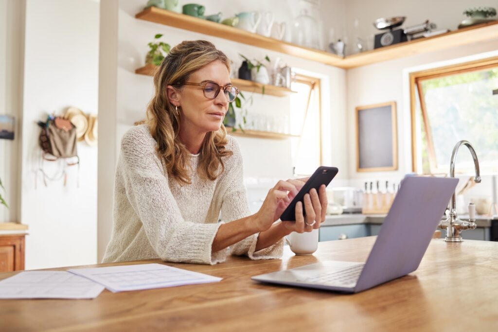 Woman looking over documents on her phone and laptop.