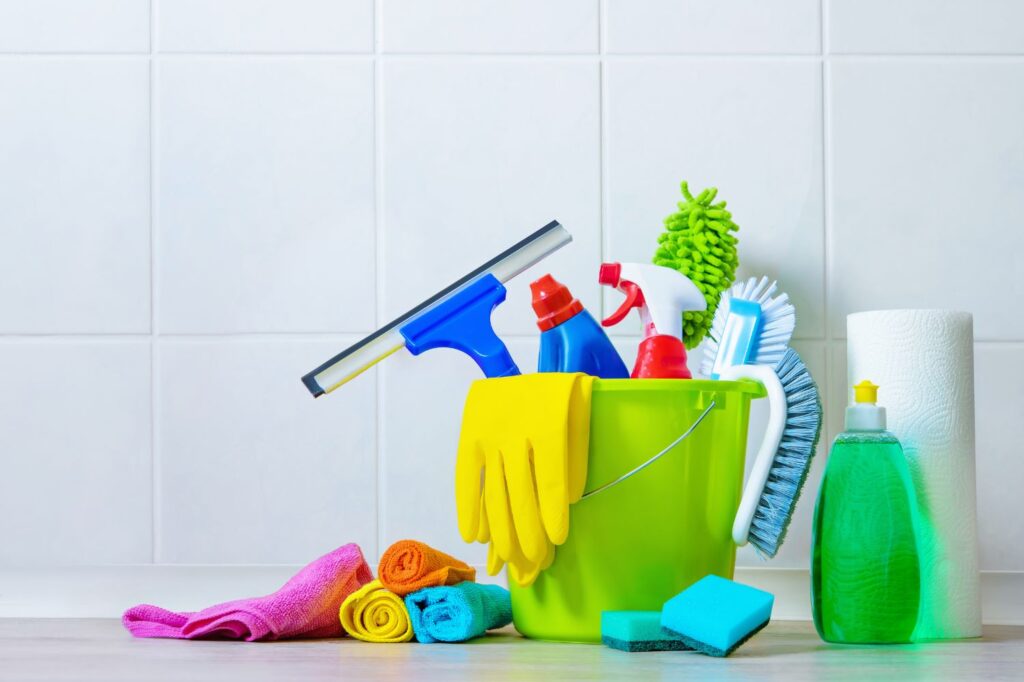 Household cleaning supplies stacked up in front of a tiled wall.