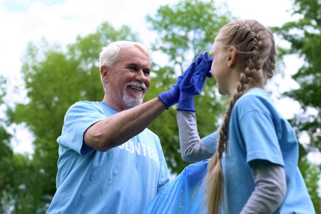 Senior man smiling while high-fiving a young woman while volunteering.