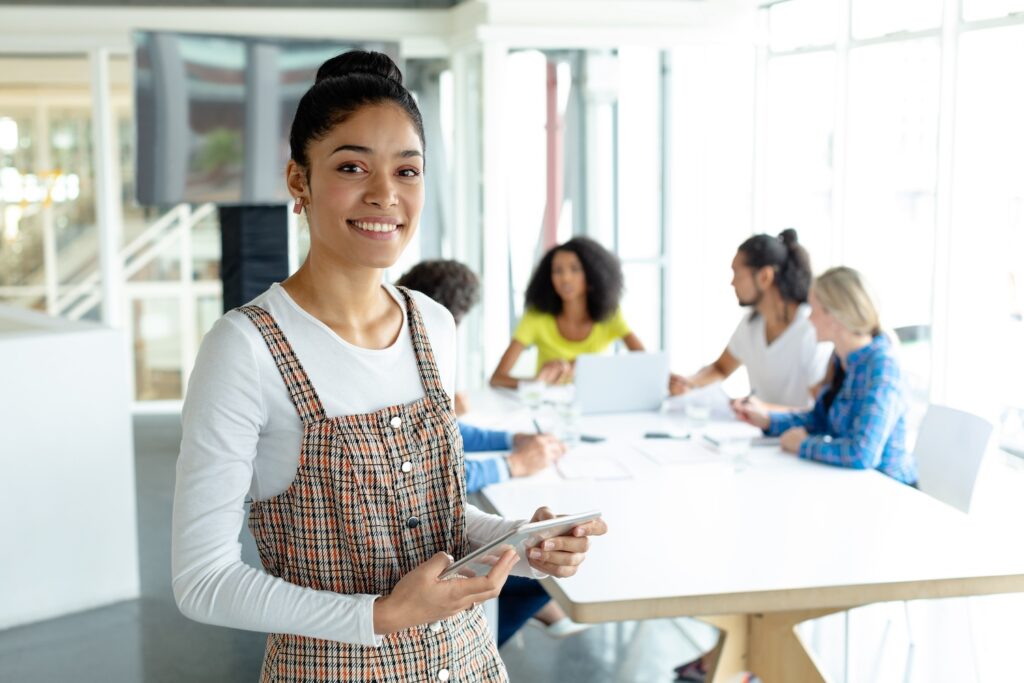 Gen Z worker smiling while standing in front of a team meeting.