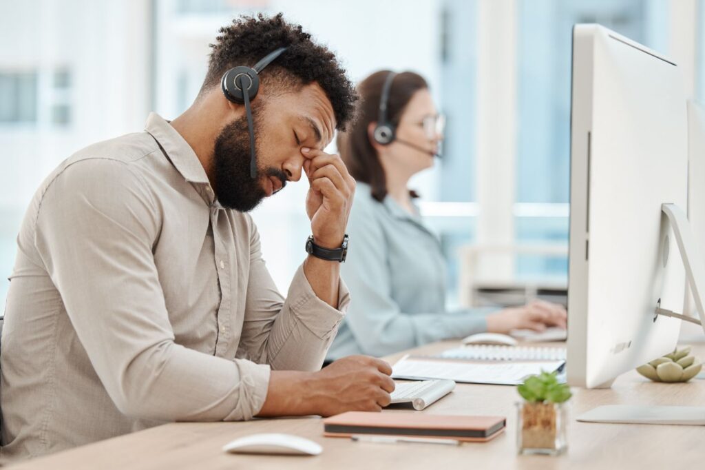 Employee with a headset on looking frustrated or burnt out at work.