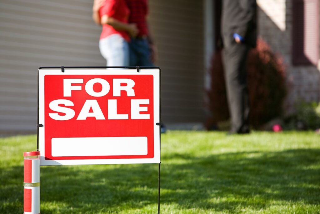 Home for sale sign in front of a couple and an agent.