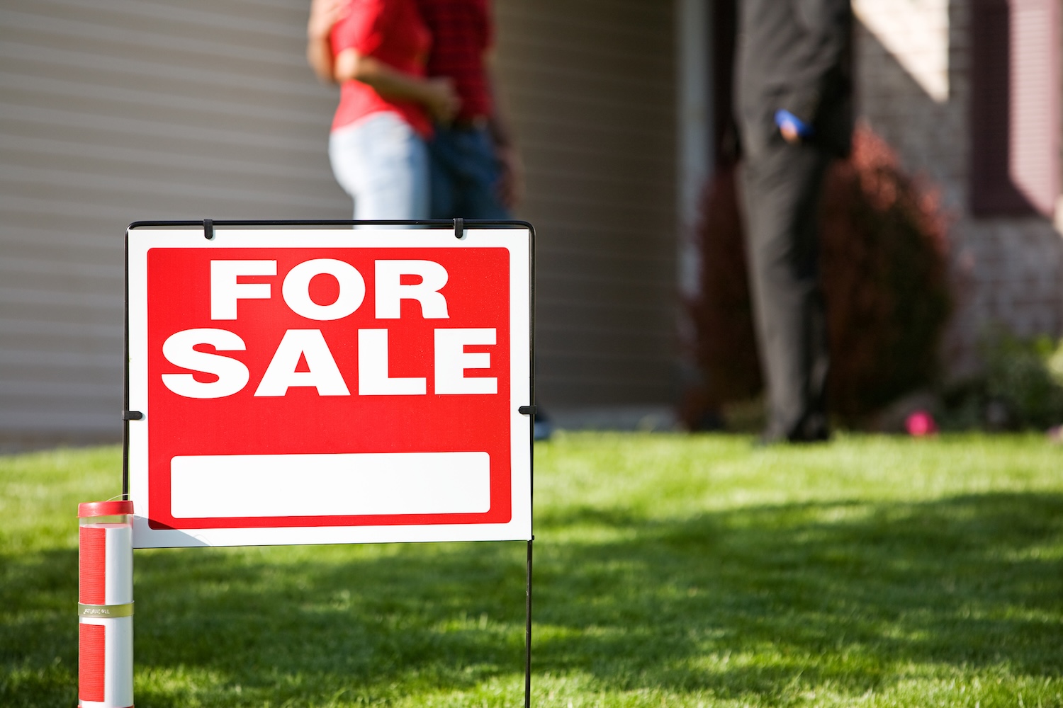 Un cartel de "Se vende" frente a una pareja y un agente inmobiliario.
