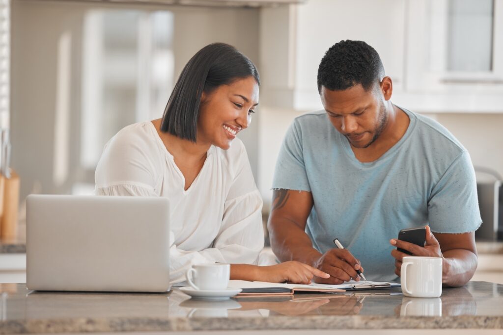 Couple smiling while looking over paperwork at a kitchen counter.