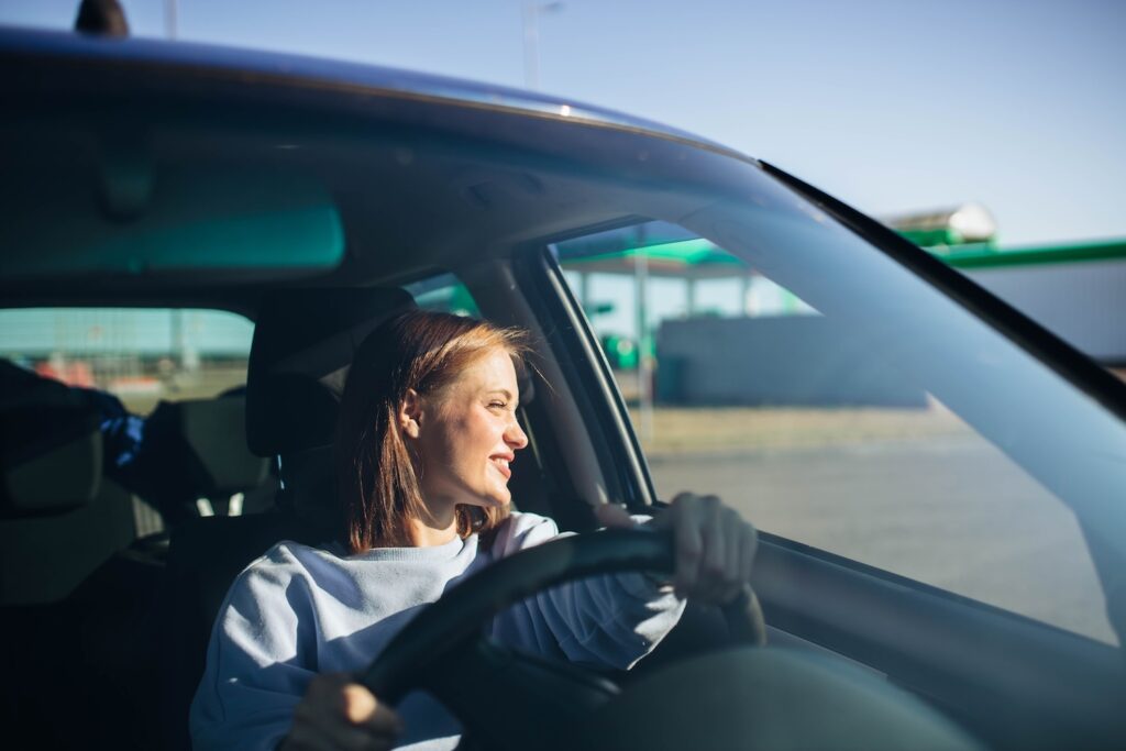 Young woman smiling while looking out her car window.