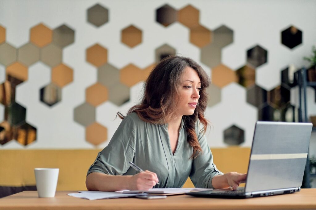 Woman looking at her laptop while writing things down.