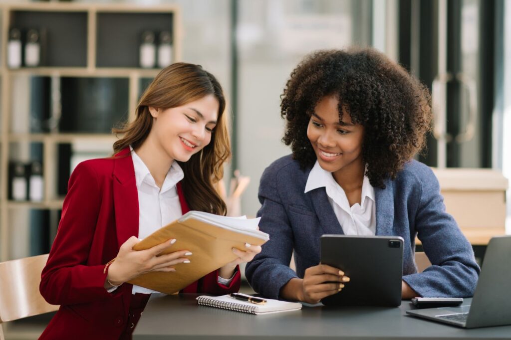 Two young women sitting together and looking over paperwork and a tablet.