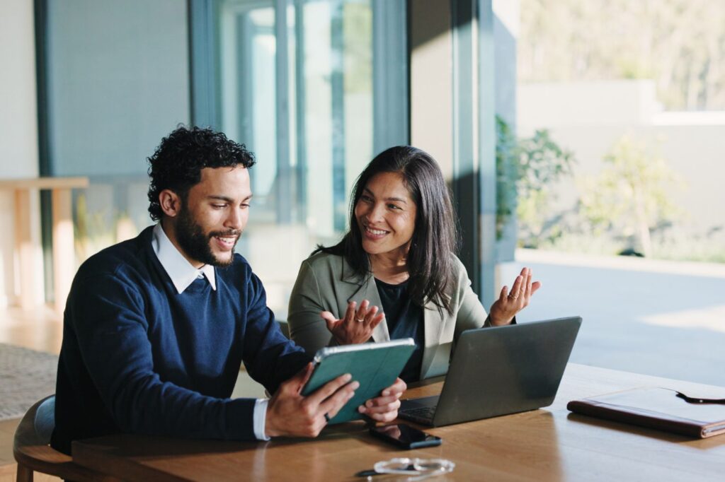 Man and woman sitting together and looking over a tablet and laptop.