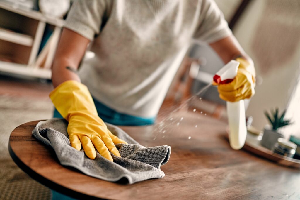 Person's hands cleaning a table while wearing gloves.