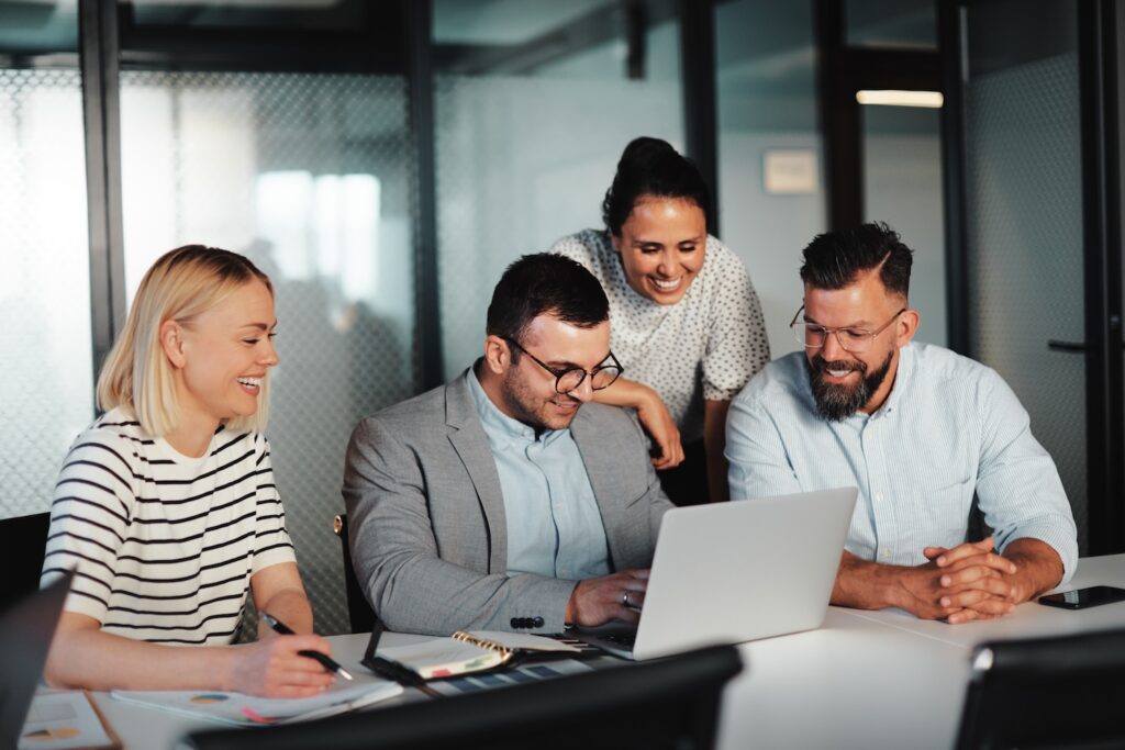 Coworkers sitting together and smiling while looking at a laptop.