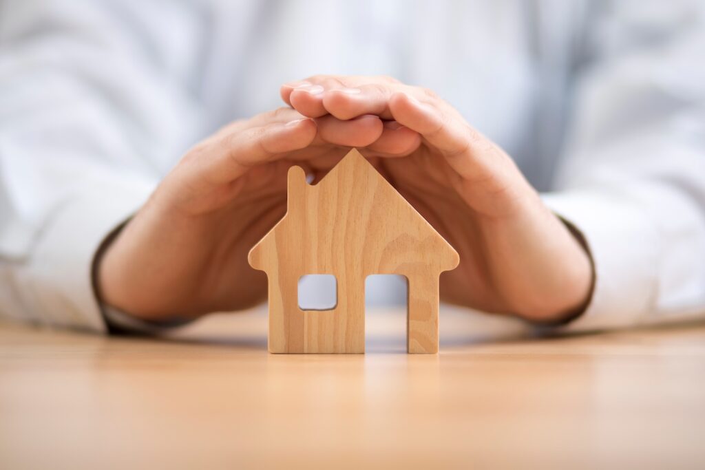 Person's hands protecting a wooden house.