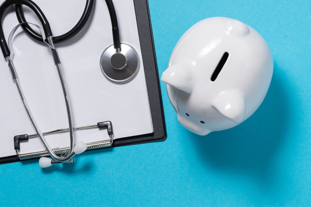 Clipboard with a stethoscope on it next to a piggy bank.