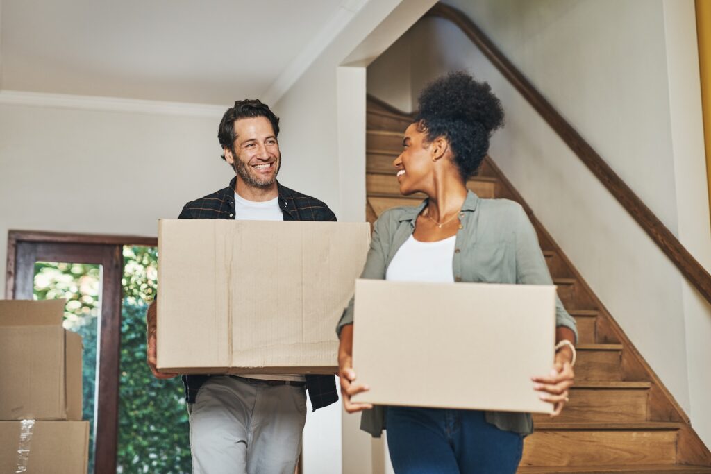 Couple smiling while carrying moving boxes.