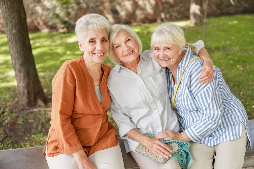 Three mature women sitting together and smiling in a park.