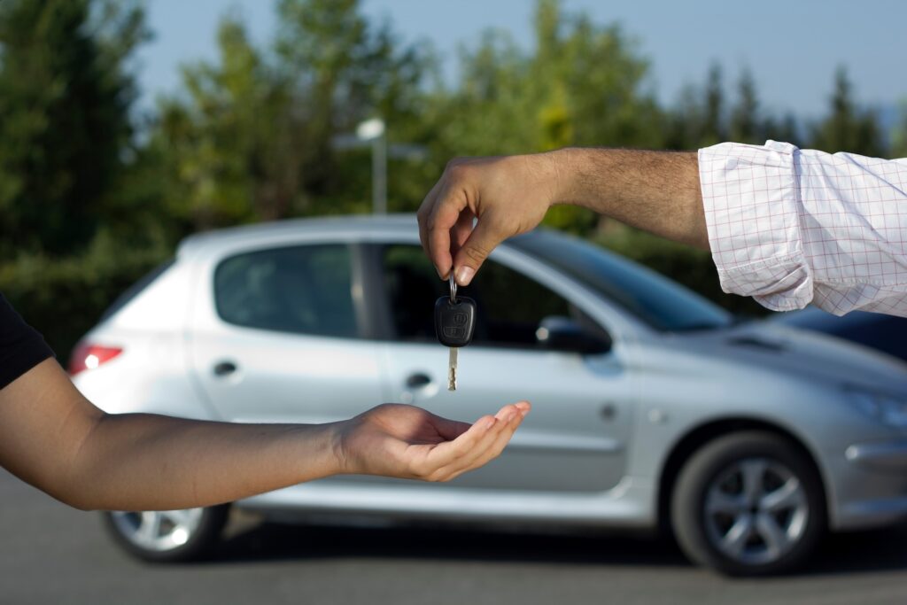 Person handing over a car key in front of a used car.
